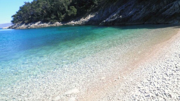 A pebble beach with clear turquoise water and a rocky cliff with trees. - Holiday apartment with outdoor pool, sauna and hot tub (Drenje)
