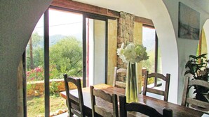 A dining area with a table and chairs, a vase with flowers, and a view of greenery and mountains through large windows. - Amazing apartment in Partinello (Partinello)