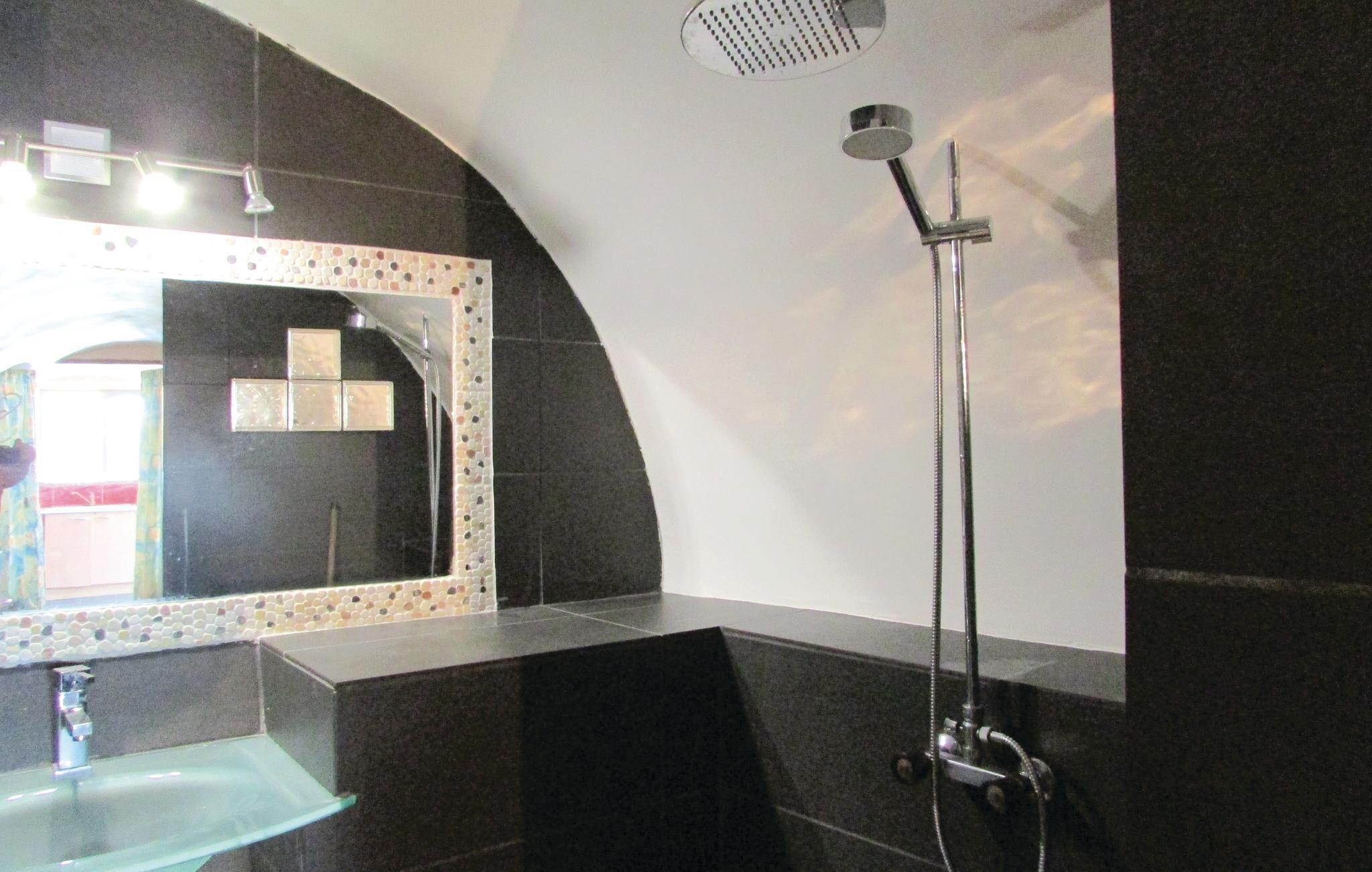 Un baño moderno con un espejo curvo, un lavabo de vidrio y una ducha con cabezal de ducha de mano.