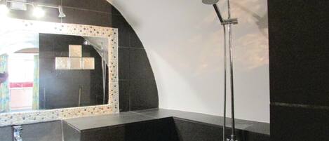 Un baño moderno con un espejo curvo, un lavabo de vidrio y una ducha con cabezal de ducha de mano.