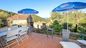 An outdoor deck with a wooden floor, a table with chairs, and two blue umbrellas. - Amazing apartment in Partinello (Partinello)