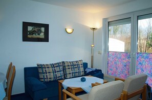 A room with a blue sofa, a small table with a blue tablecloth, a lamp, and a framed picture on the wall.