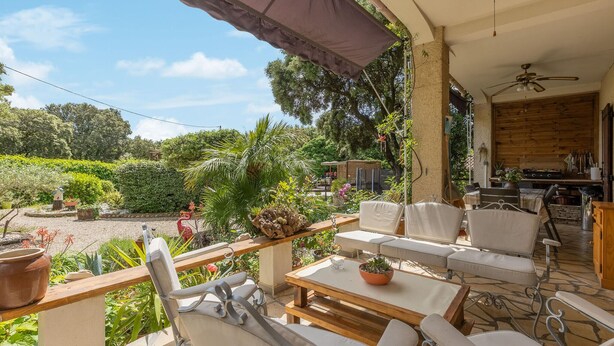 Eine Terrasse mit Sitzgelegenheiten im Freien, einem Holztisch und einem Deckenventilator.