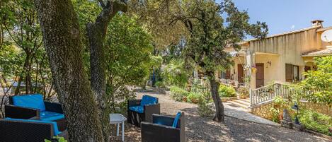 An outdoor seating area with wicker furniture and a stone pathway leading to a building with a tiled roof.