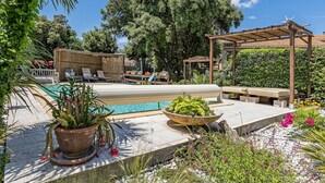 Ein Poolbereich mit Liegestühlen, einer Pergola und einem Garten mit Blumentöpfen und Blumen.