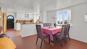A bright kitchen with white cabinets, a wooden island, and a dining area with wicker chairs and a pink tablecloth. - Gorgeous home in Fanø with kitchen (Fanø)
