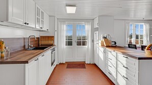A kitchen with white cabinets, a wooden countertop, a sink, and a window with curtains. - Gorgeous home in Fanø with kitchen (Fanø)