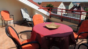 Una terraza con una mesa roja, sillas naranjas y una cesta de mimbre.
