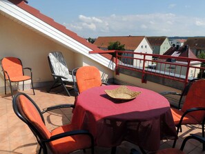 A terrace with a red table, orange chairs, and a wicker basket.