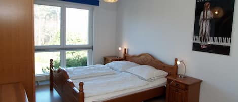 A bedroom with a double bed, bedside tables, a hanging light fixture, a window, and a poster on the wall.
