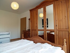 A bedroom with a wooden bed, a dresser, and a wardrobe with a mirror.