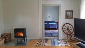 Una habitación acogedora con una estufa de leña, una cama con una manta azul, una alfombra colorida y un huso.