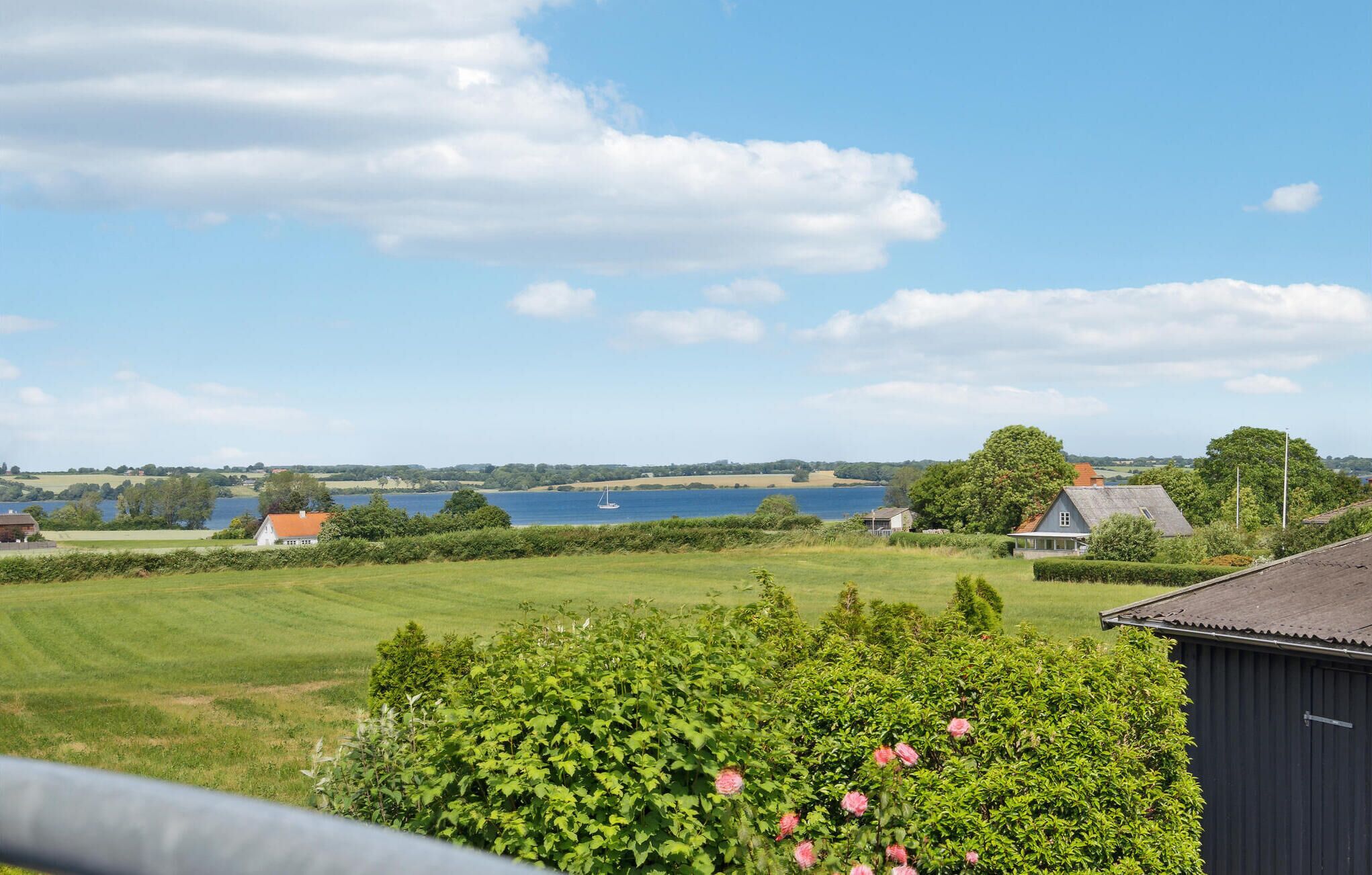 A rural landscape with a large field, a body of water, and a few houses.