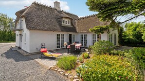 A white house with a thatched roof, a covered patio with a table and chairs, and a garden with various plants and a tree. - 3 bedroom stunning home in Sydals (Sydals)