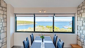 A dining area with a table and chairs, a large window with a view of a body of water and a yacht, and stone walls. - 4 bedroom amazing home in Tankaraca (Tankaraca)