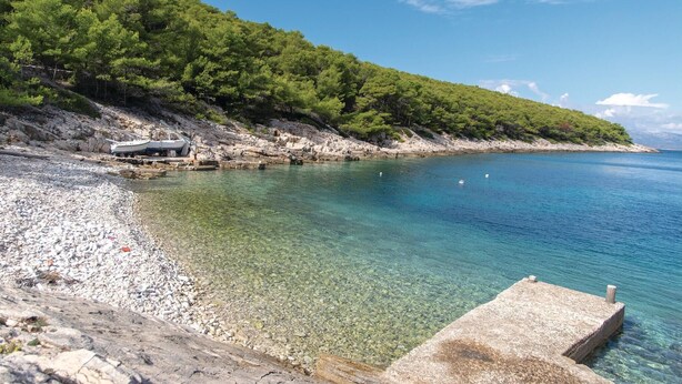 A rocky beach with clear water, a boat, and a forested hill. - 4 bedroom amazing home in Tankaraca (Tankaraca)