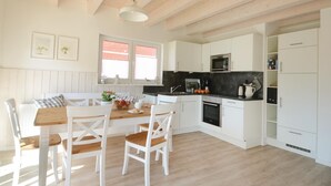 A bright kitchen with white cabinetry, a wooden dining table, and a window with blinds. - Stunning home in Süssau/Ostsee (Süssau/Ostsee)
