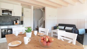 A modern kitchen with white cabinets, a built-in oven, and a dining area with a wooden table, chairs, and a bowl of fruit. - Stunning home in Süssau/Ostsee (Süssau/Ostsee)