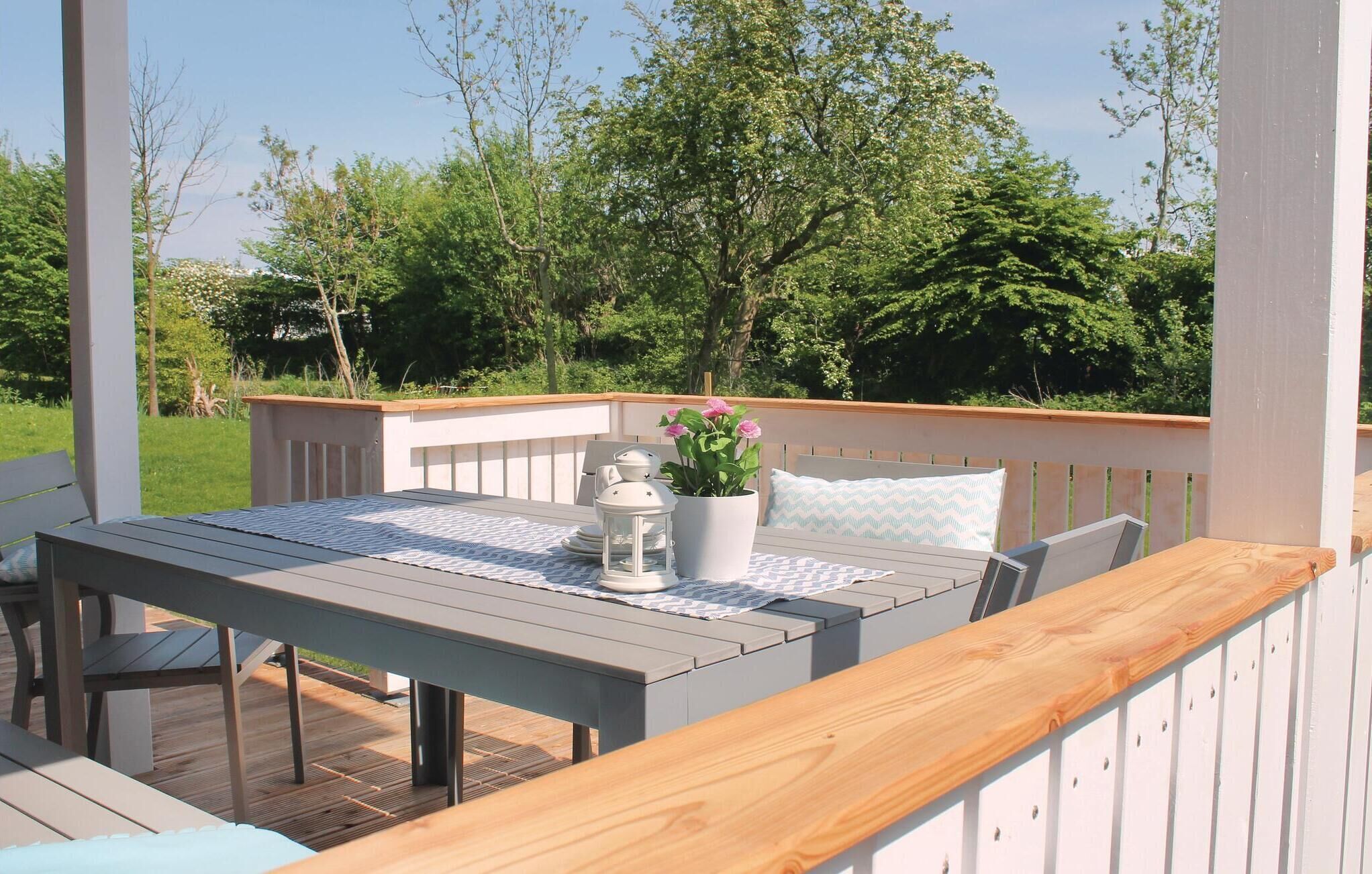 Een houten terras met een tafel, stoelen, een plant in pot en een lantaarn.