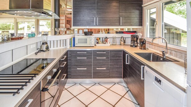 A modern kitchen with dark cabinetry, a large window, and a built-in oven. - Cozy home in Saltum with sauna (Saltum)