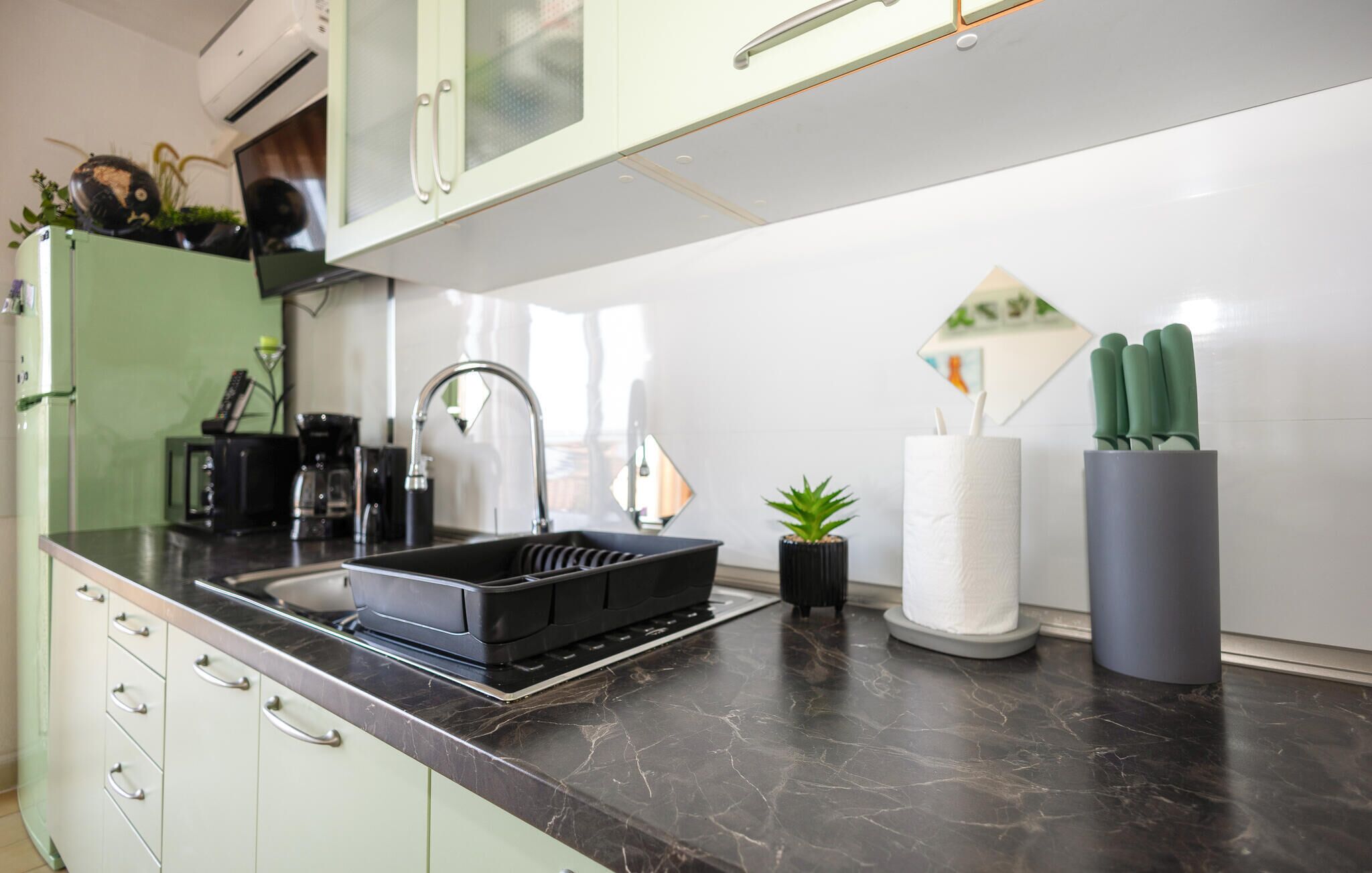 Een keuken met een zwart aanrecht, een spoelbak, een koffiezetapparaat en een kleine pot met een plantje.
