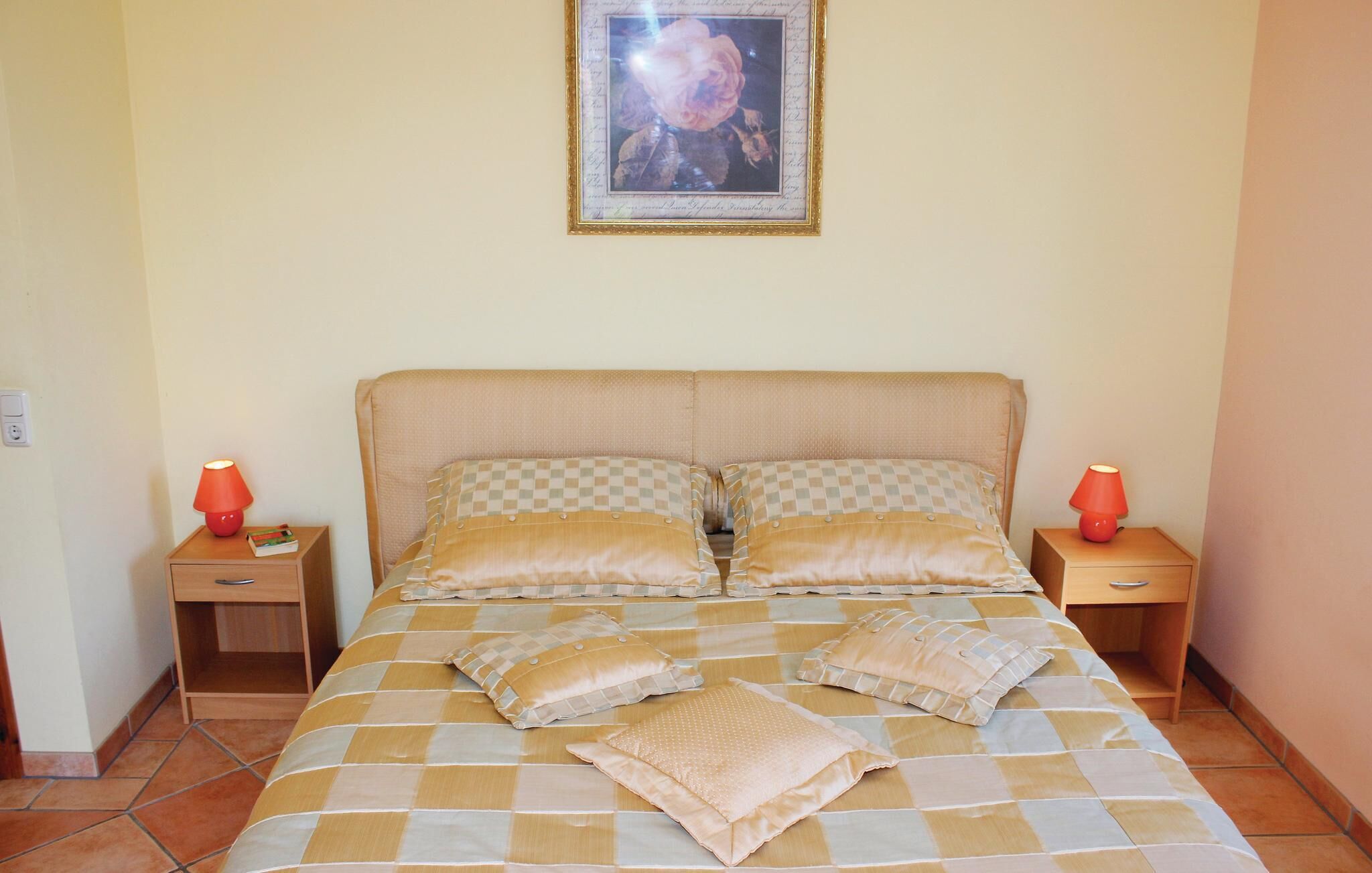 Cama bem arrumada com colcha xadrez e várias almofadas, duas mesas de cabeceira com abajures e um quadro emoldurado na parede.
