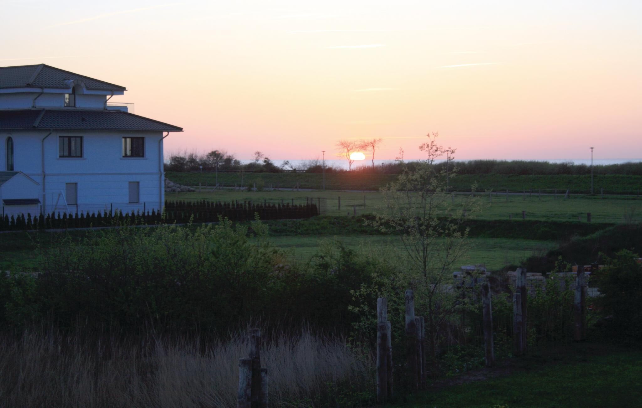 A white building with a flat roof and multiple windows, surrounded by a grassy field and a fence.