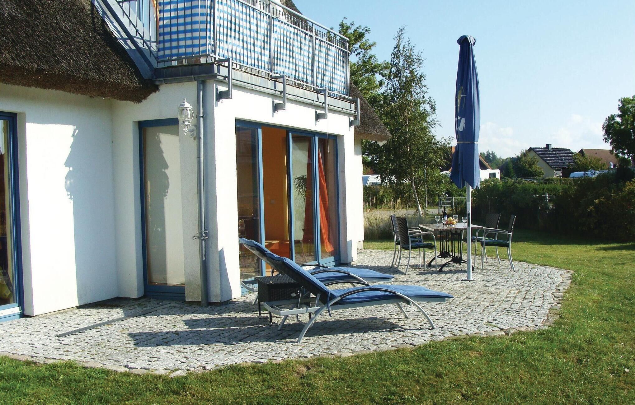 Une maison moderne dotée d’un balcon, d’une terrasse avec des fauteuils et d’une table sur laquelle se trouvent une bouteille et des verres.