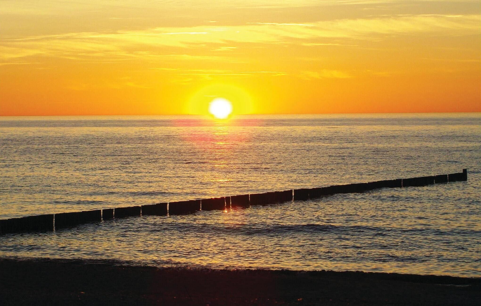 Ein Sonnenuntergang über einem ruhigen Meer mit einer anlegenden Mole.