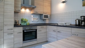 A modern kitchen with light wood cabinets, a built-in oven, a microwave, and a kettle. - Plötz Vacation Rental - with a Sun Terrace and Electric Car Charging Station - Vacation Rental with (Loddin)