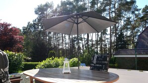 A round wooden table with a metal frame, an umbrella, and a sign with words on it. - Plötz Vacation Rental - with a Sun Terrace and Electric Car Charging Station - Vacation Rental with (Loddin)