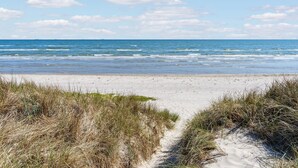 Uma praia com areia e grama ao primeiro plano, que se estende até o oceano.