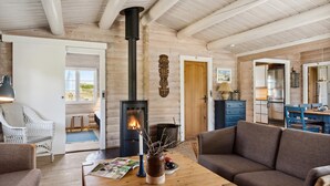 Interior acolhedor de cabana com lareira a lenha, área de jantar com mesa de madeira e sala de estar com sofá.