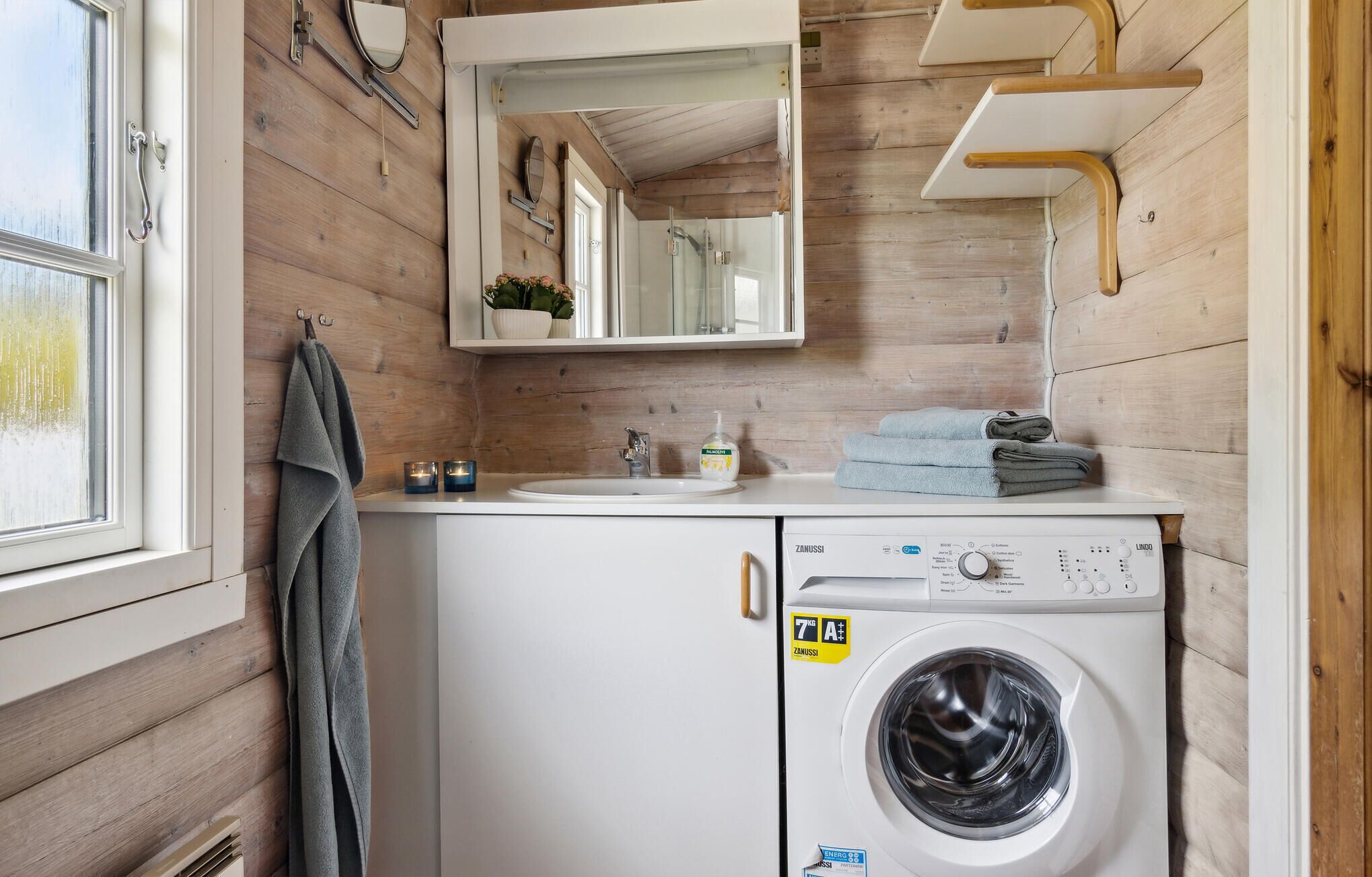 A compact bathroom with a washing machine, a sink, and a mirror.