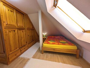 A bedroom with a sloped ceiling, wooden wardrobe, and a bed with a colorful bedspread. - Holiday apartment with garden, balcony and air conditioning (Balatonfenyves)