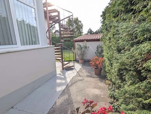 A residential area with a staircase leading to a second floor, a potted plant, and a hedge.