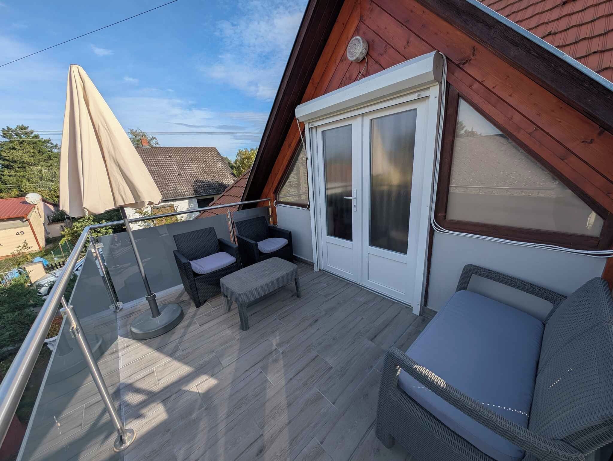 A balcony with a glass balustrade, wicker furniture, and a sliding glass door leading to an outdoor area.
