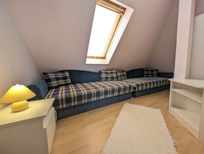 A cozy loft bedroom with a skylight, a sofa bed, a bedside table with a lamp, and a white rug. - Holiday apartment with garden, balcony and air conditioning (Balatonfenyves)