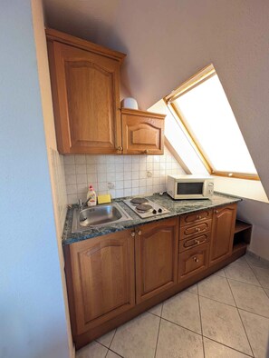 A kitchen with wooden cabinets, a microwave, a sink, and a window.