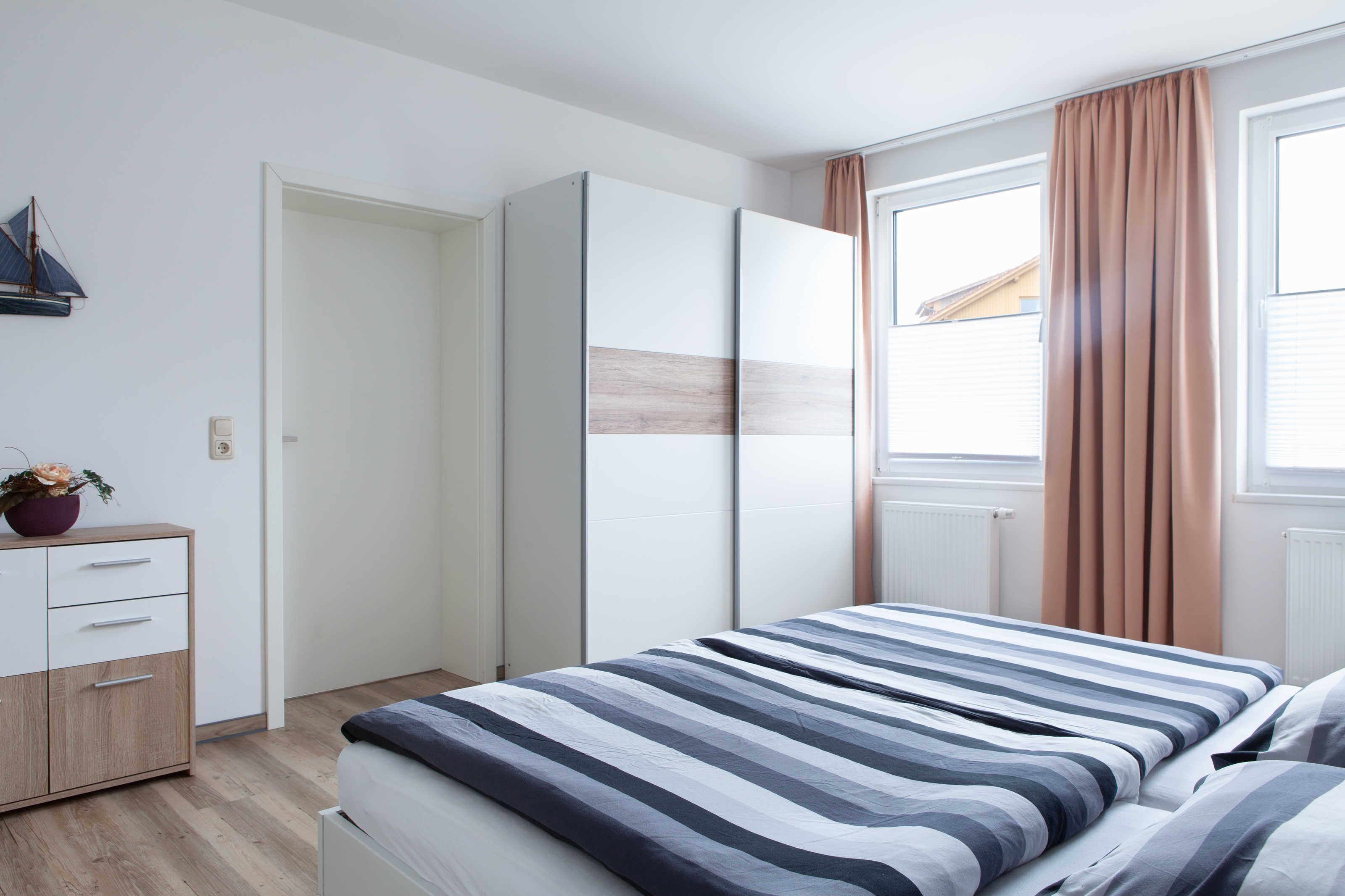 A bedroom with a bed, a wardrobe, a dresser, and a window with curtains.