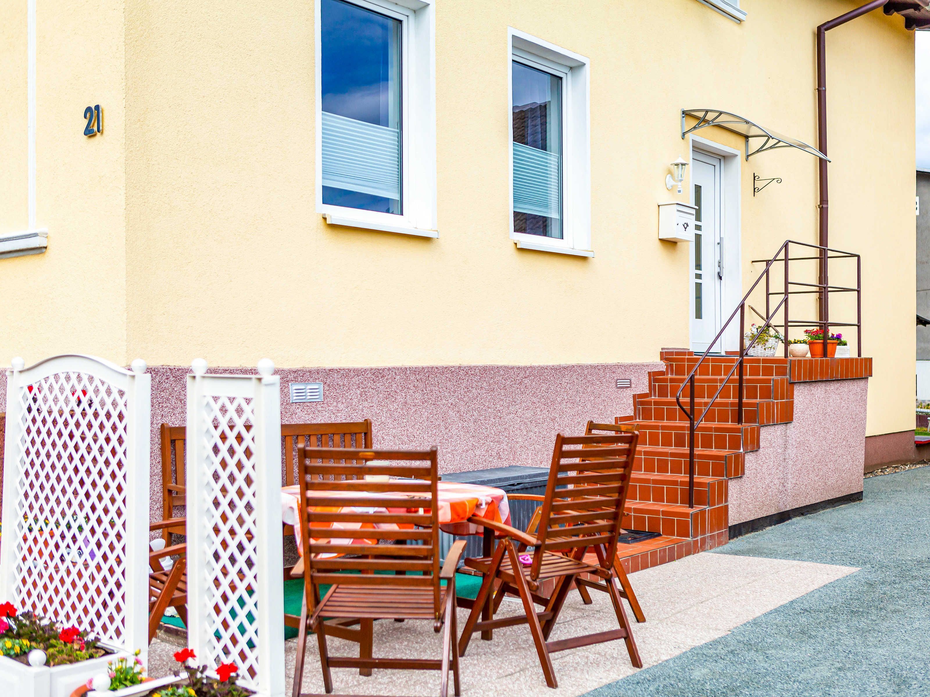 Un edificio amarillo con un cartel con el número 21, una escalera y una terraza con sillas y mesa de madera.