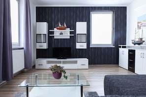 Una sala de estar moderna con una mesa de centro de vidrio, un televisor de pantalla plana y un estante decorativo con maquetas de barcos.