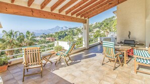 Un patio esterno coperto con mobili in legno, un barbecue e vista su un paesaggio montuoso.