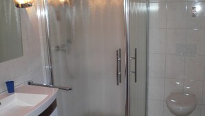Moderni kylpyhuone, jossa on lasinen suihkuseinä, valkoinen pesuallas ja wc-istuin.