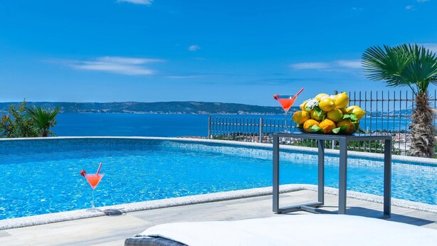 A poolside area with a table holding lemons and a martini glass, overlooking a clear blue sea. - Luxurious home in Kastel Kambelovac with sauna (Kastel Kambelovac)