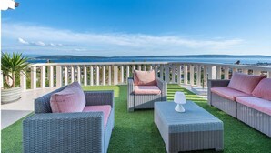 A terrace with wicker furniture, a white railing, and a view of the sea. - Luxurious home in Kastel Kambelovac with sauna (Kastel Kambelovac)