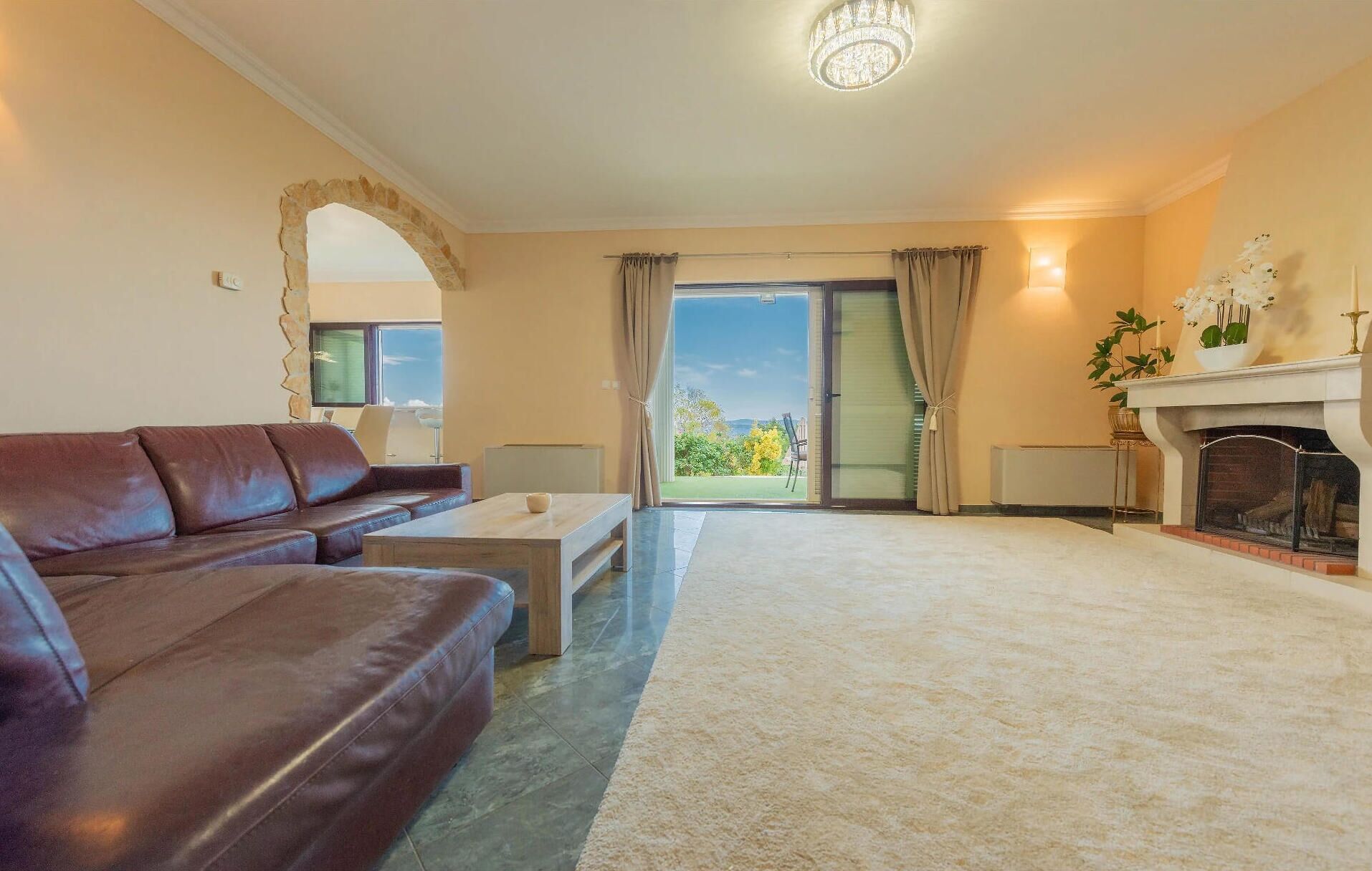 Un salon avec un canapé en cuir marron, une table basse, une cheminée et une vue sur un espace extérieur, visible à travers une porte vitrée.
