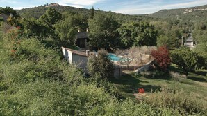 Ein Pool, umgeben von üppigem Grün, ein Steinhaus und eine Hügelkulisse mit einer schlossartigen Struktur im Hintergrund.