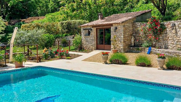 Ein Steinhaus mit Swimmingpool, umgeben von Grünpflanzen und Blumen.