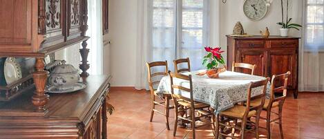 A dining area with a round table, wooden chairs, a patterned rug, a clock, and a cabinet with decorative items.